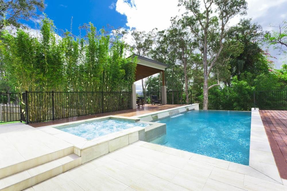 A Large Swimming Pool With A Hot Tub In The Backyard Surrounded By Trees — Rockscene Pools in Bentley Park, QLD
