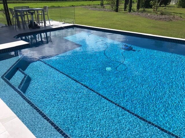 A Large Swimming Pool With a Table and Chairs in the Background — Rockscene Pools in Bentley Park, QLD