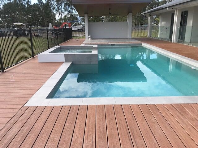 A Large Swimming Pool With a Wooden Deck Surrounding It — Rockscene Pools in Bentley Park, QLD