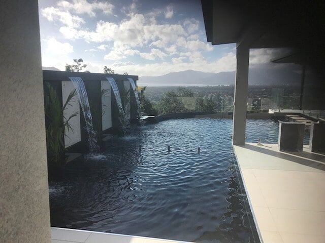A Large Swimming Pool With a Waterfall in the Backyard of a House — Rockscene Pools in Bentley Park, QLD