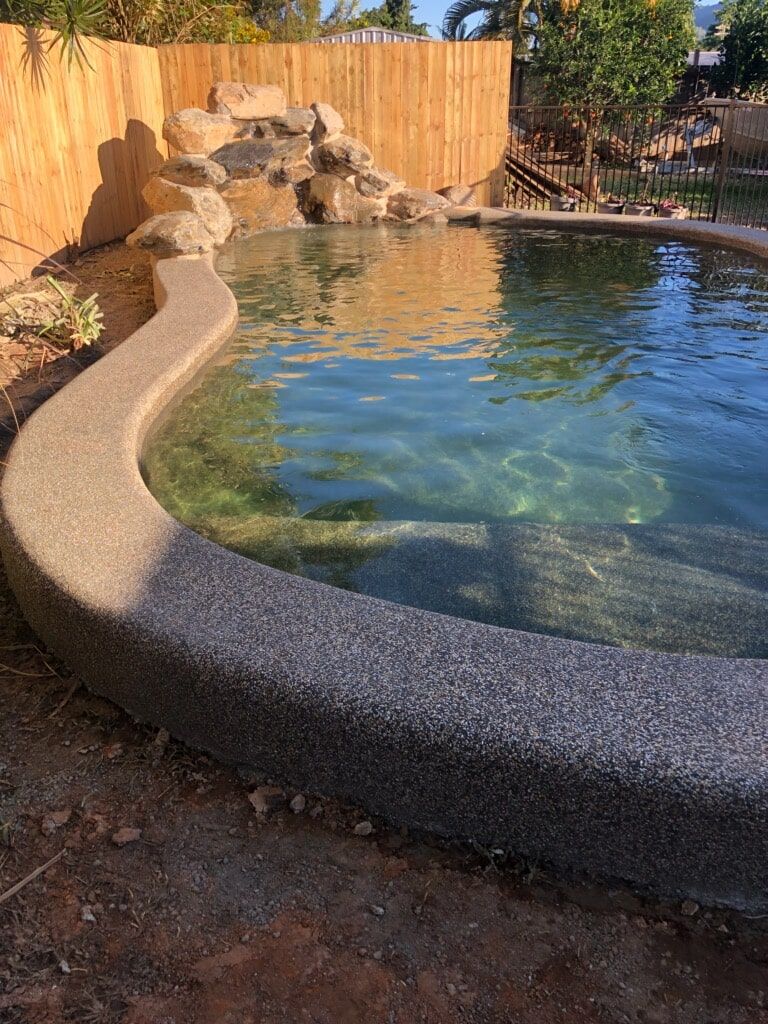 A Large Swimming Pool With a Wooden Fence in the Background\ — Rockscene Pools in Bentley Park, QLD