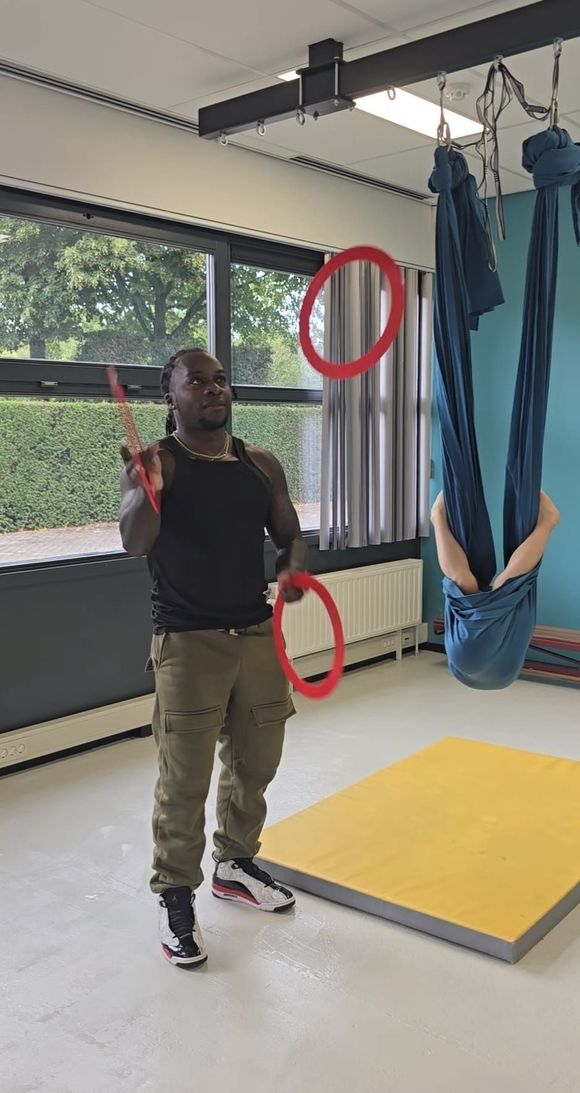 Een man staat in een kamer met drie ringen te jongleren