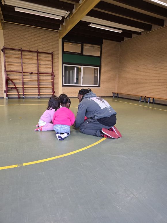 Een man geeft kinderen les op de grond in een gymzaal