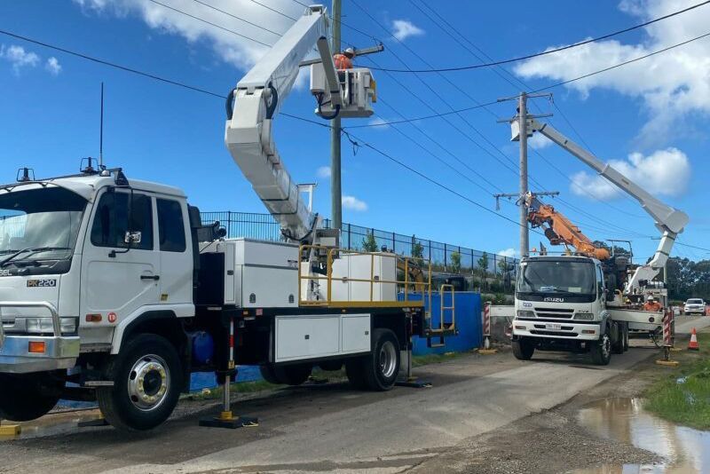 A man in a bucket is working on a power pole next to a truck.
