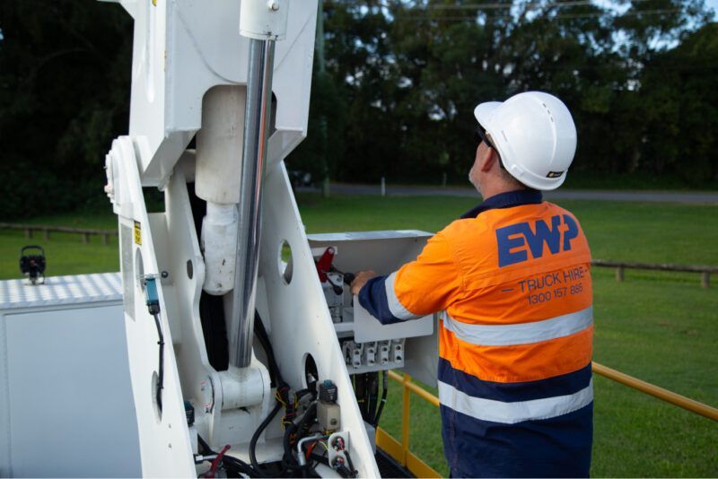 A man wearing an orange ewp shirt is working on a machine