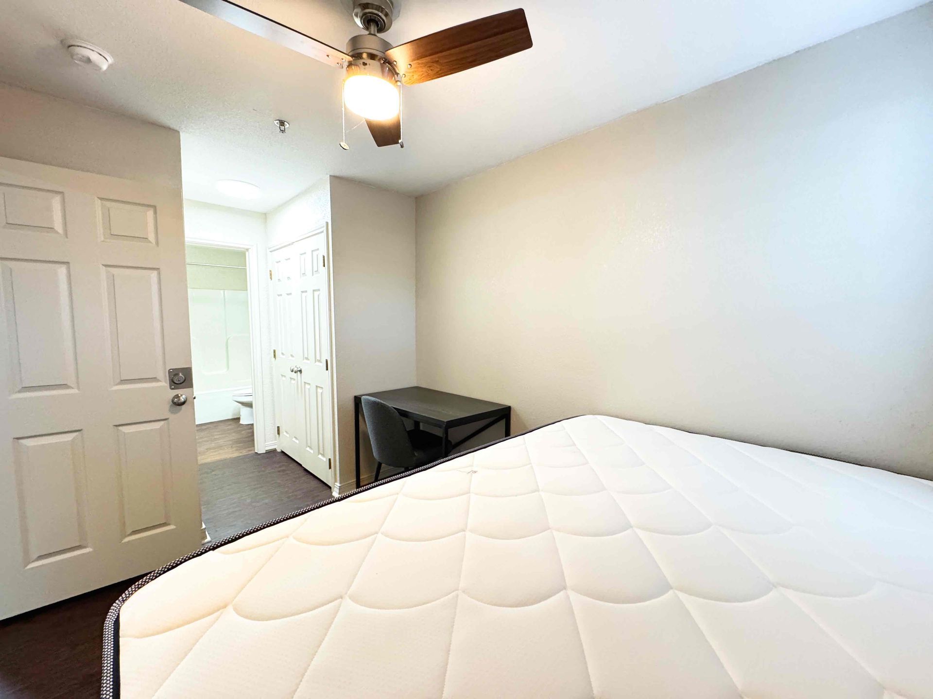 A bedroom with a bed , desk , chair and ceiling fan.