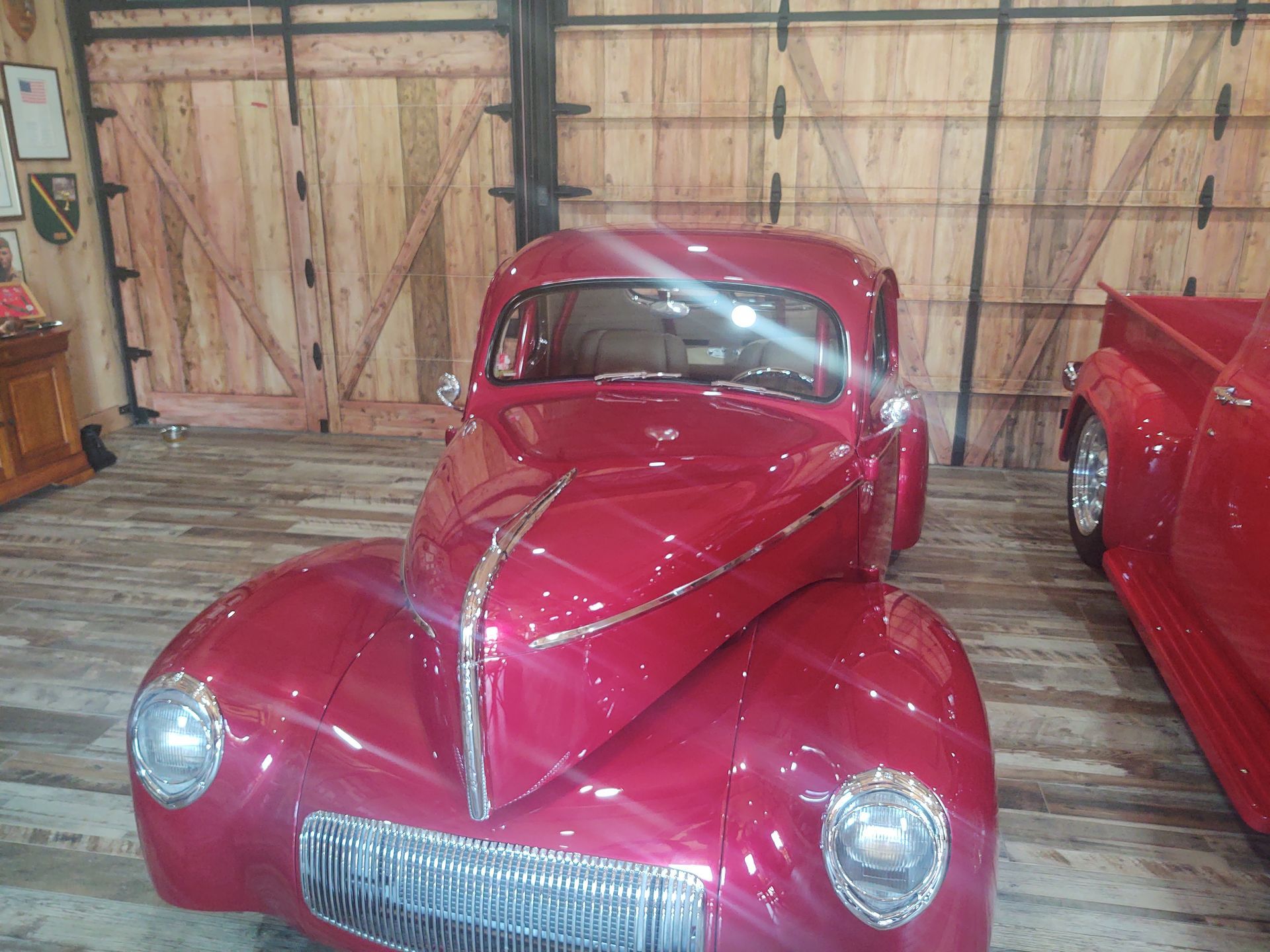 A red car is parked in a garage next to a truck.