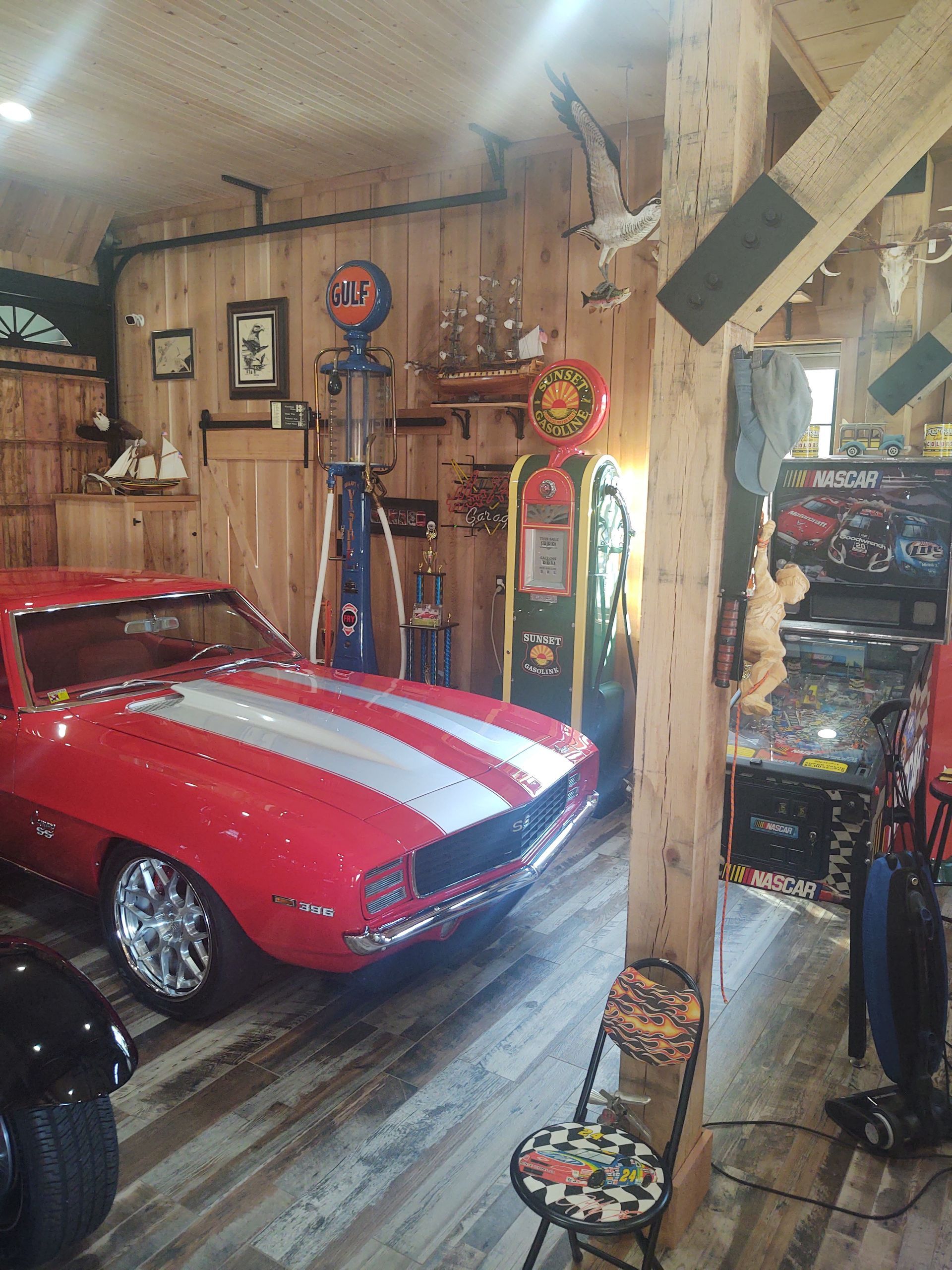 A red car is parked in a garage next to a pinball machine.