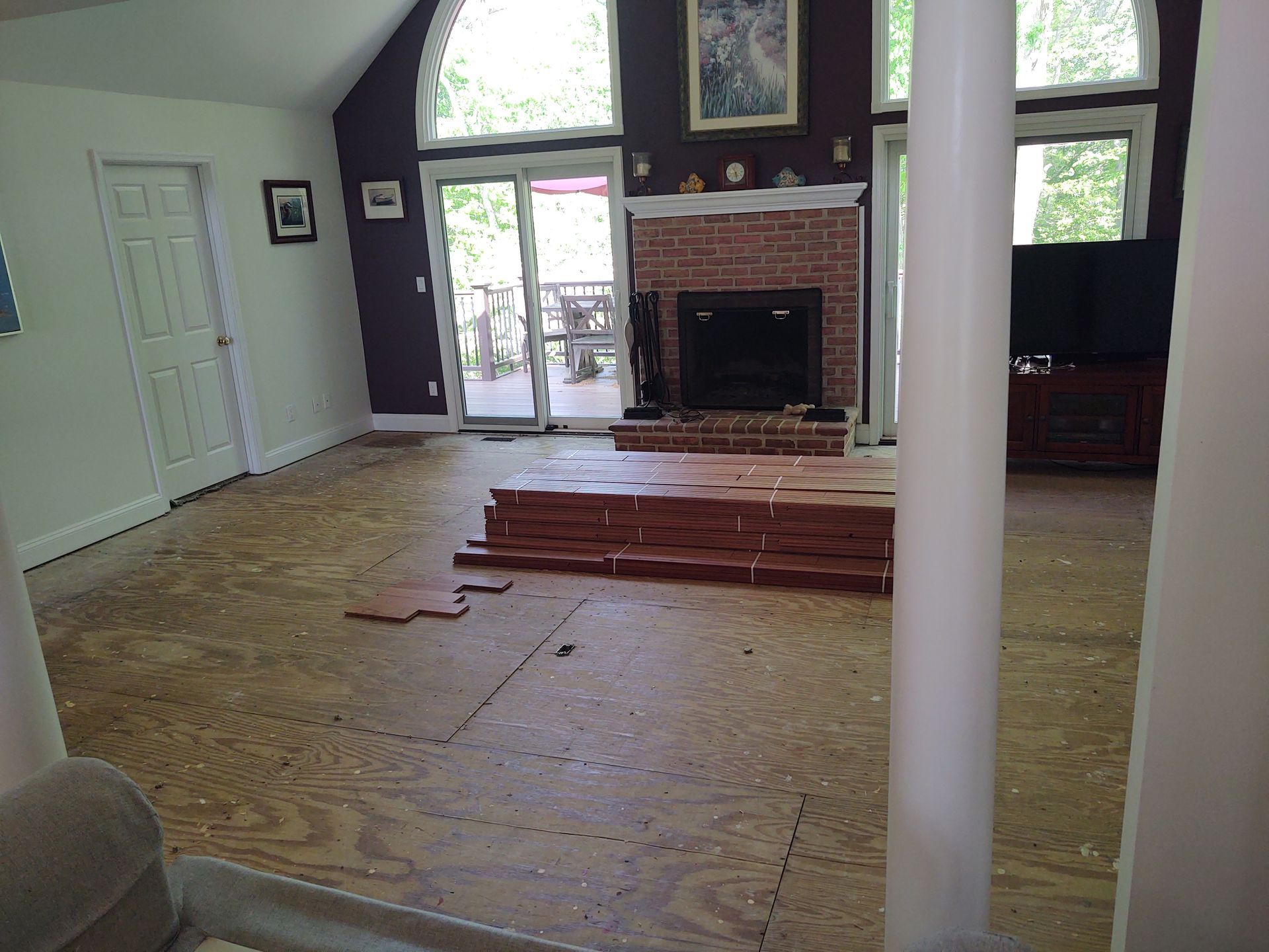 Room with plywood subfloor and stacks of wood flooring, fireplace, and sliding doors.