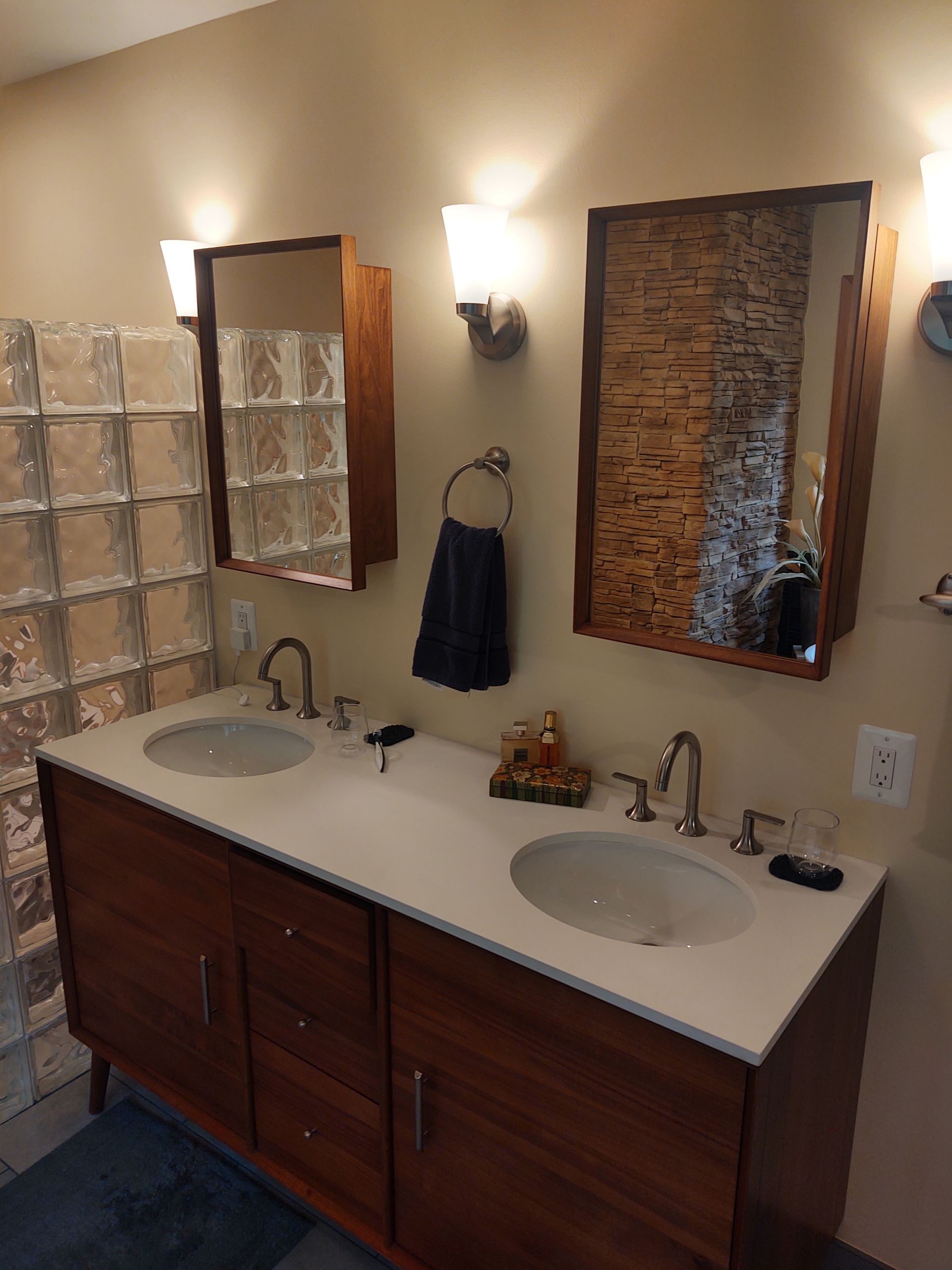 Bathroom with double sinks, two mirrors, sconces, and a glass block wall.