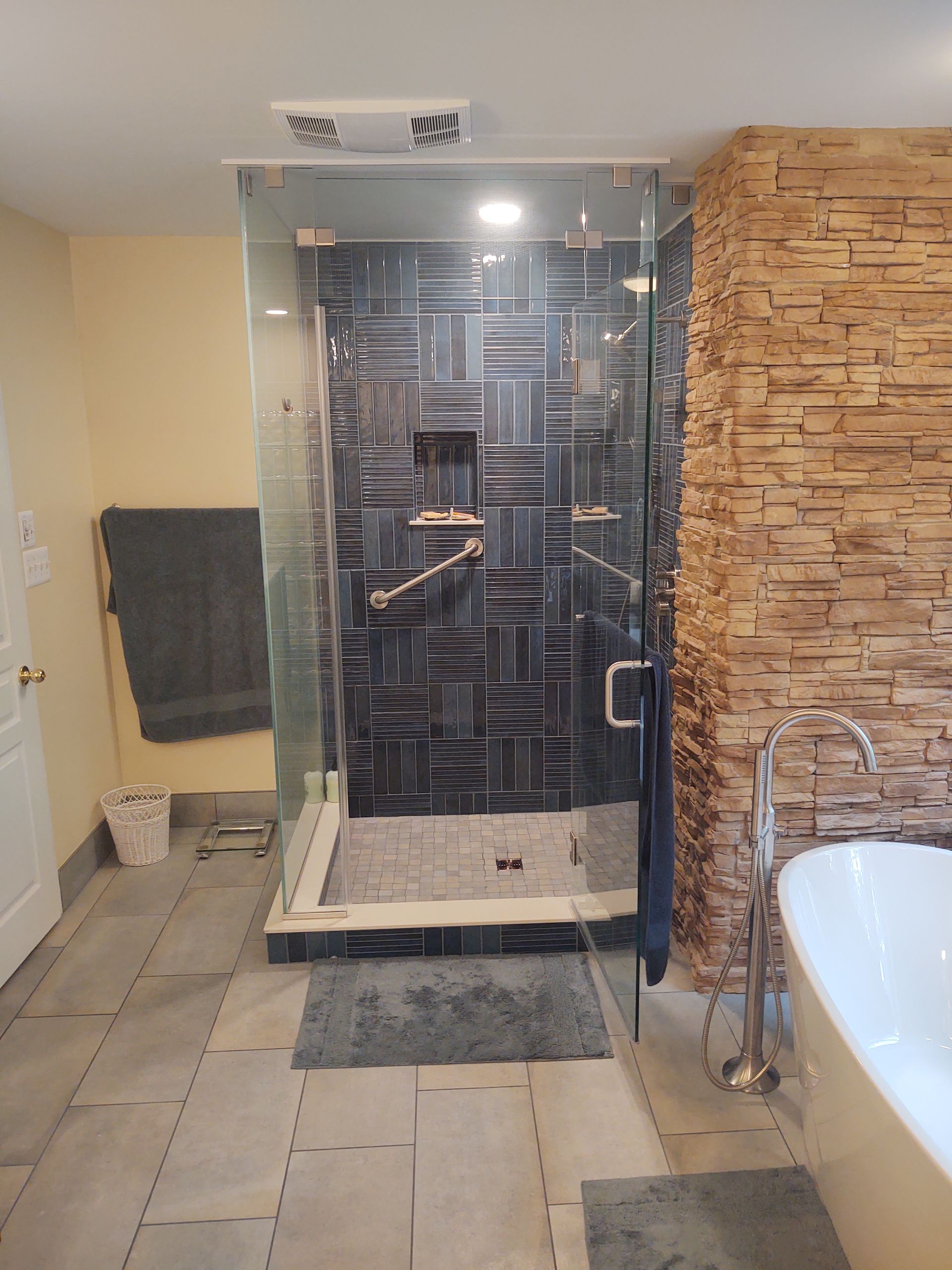 Modern bathroom with a glass-enclosed shower, stone accent wall, and a standalone tub.