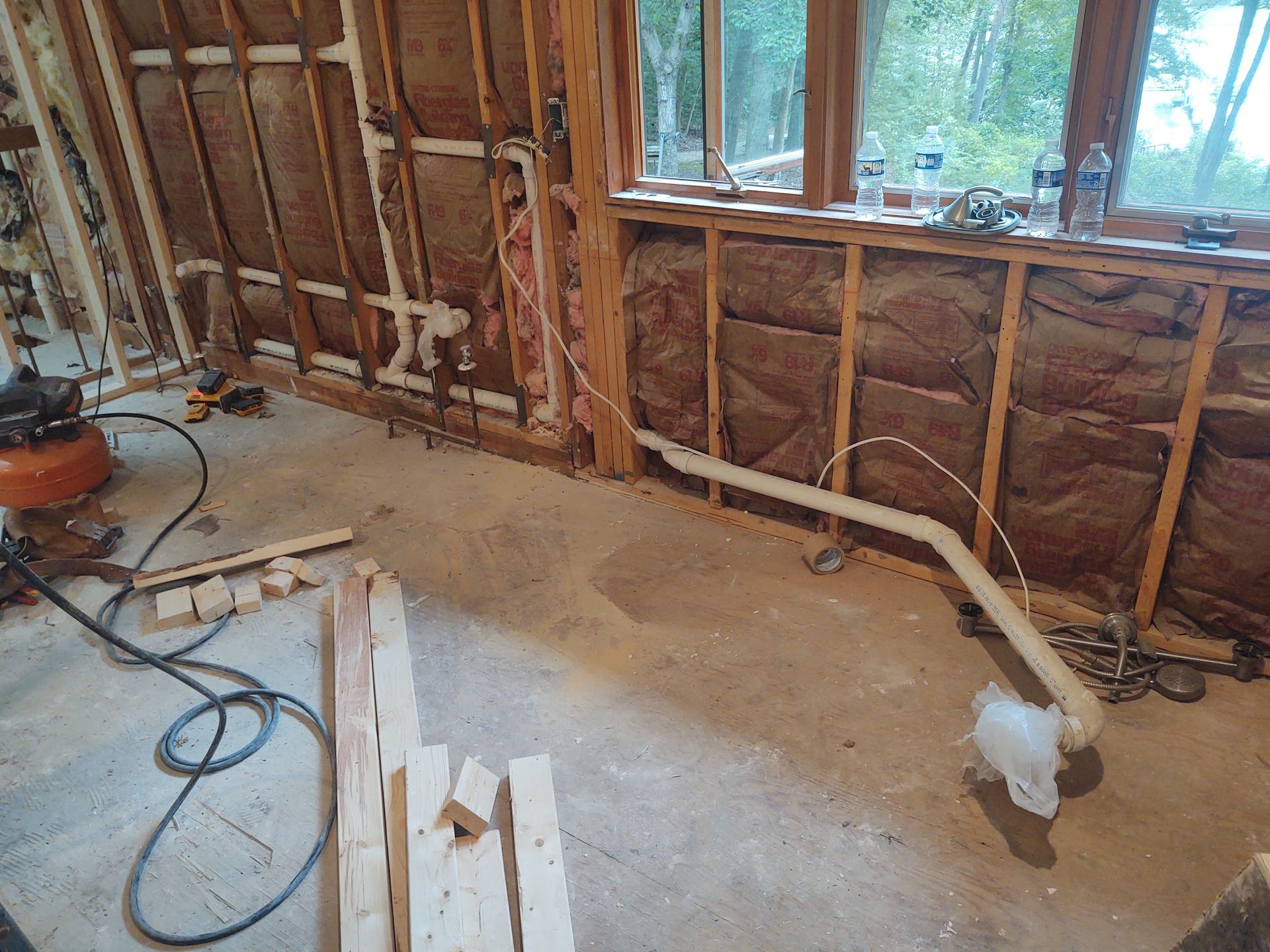 Interior construction site: exposed wall studs, insulation, plumbing, and concrete floor.