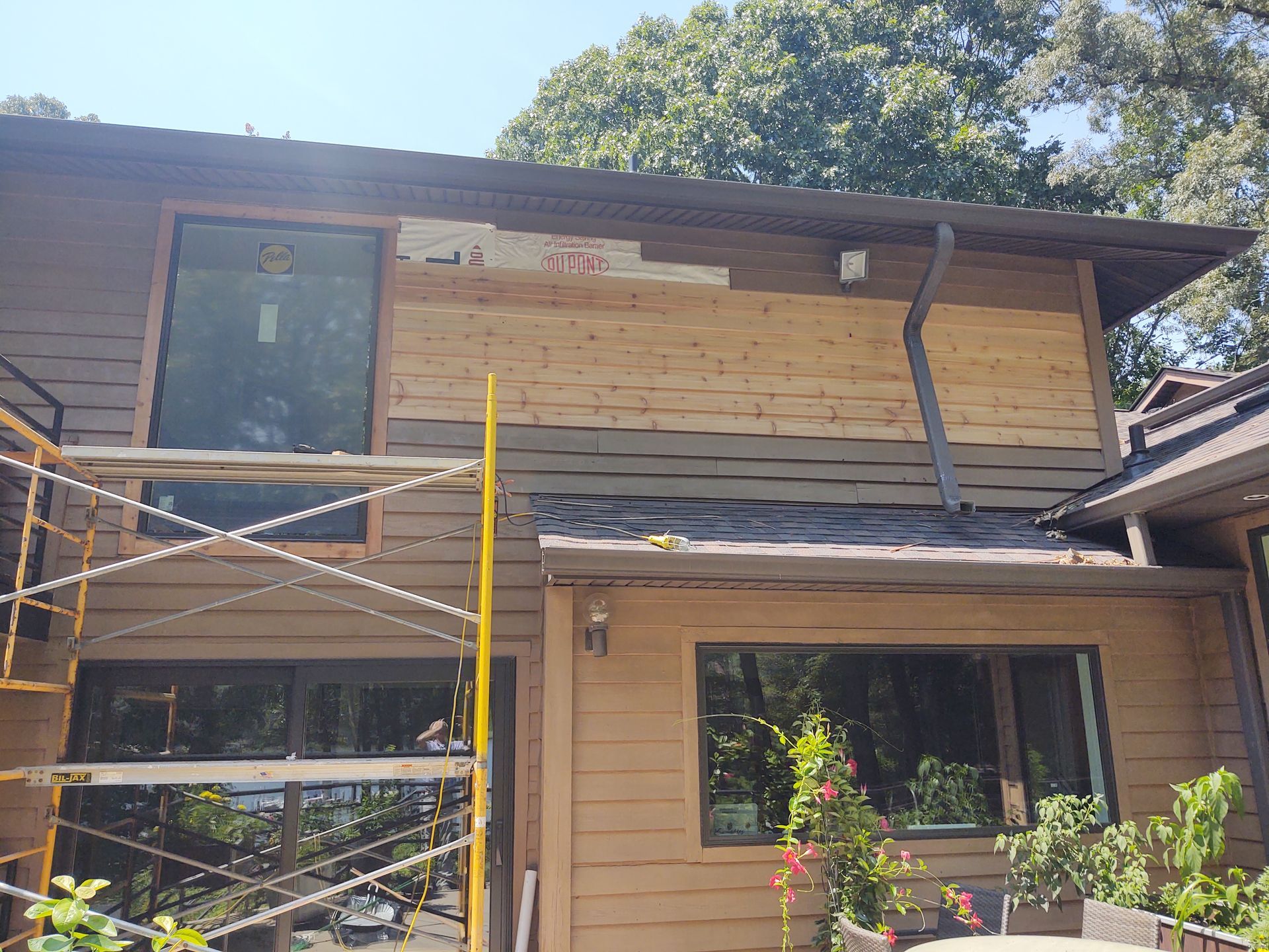 House exterior under renovation with scaffolding, showing new wood siding installed. Brown and tan colors.