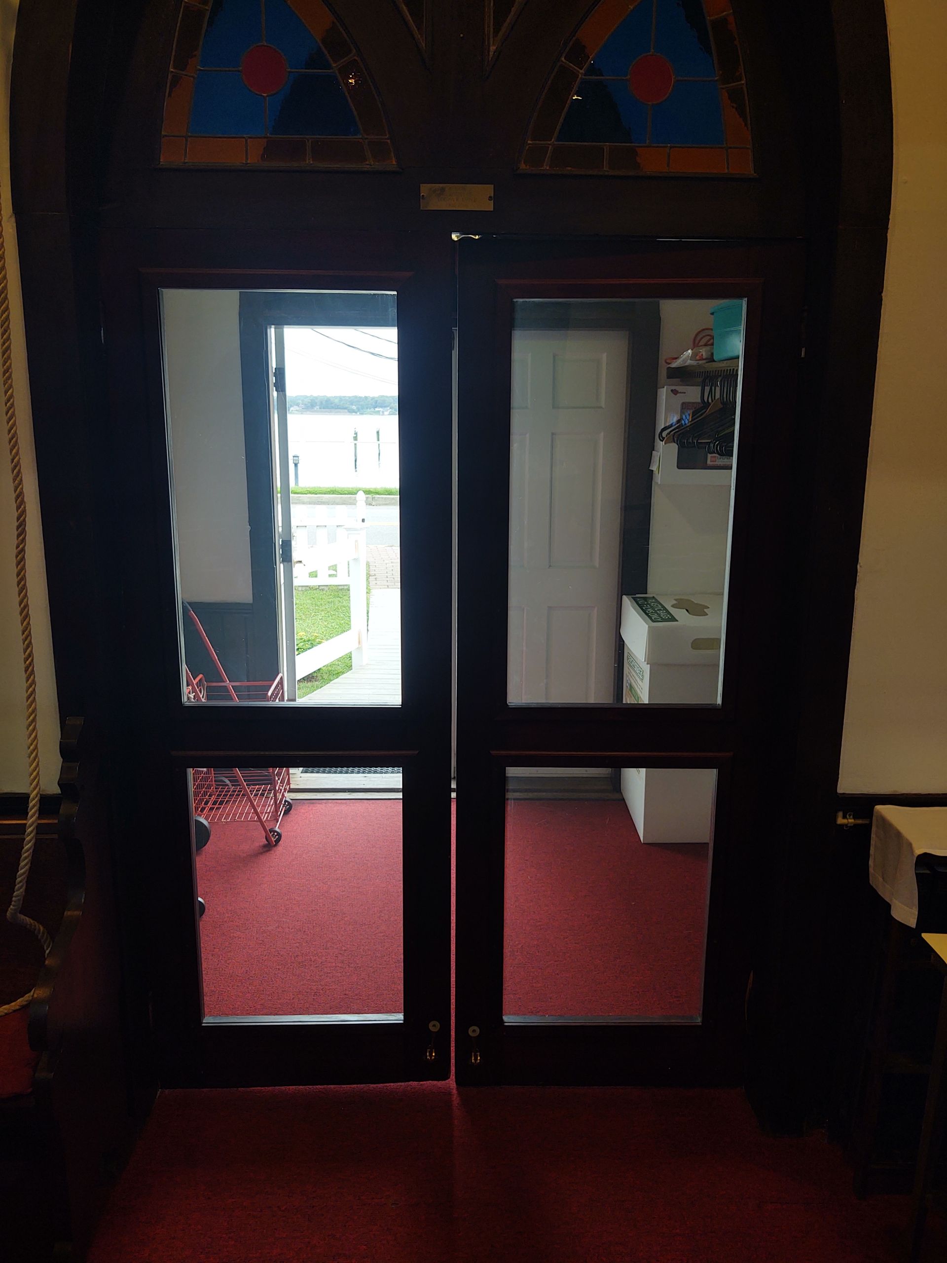 Double wooden doors with glass panes and stained glass above, opening to a hallway and outside.