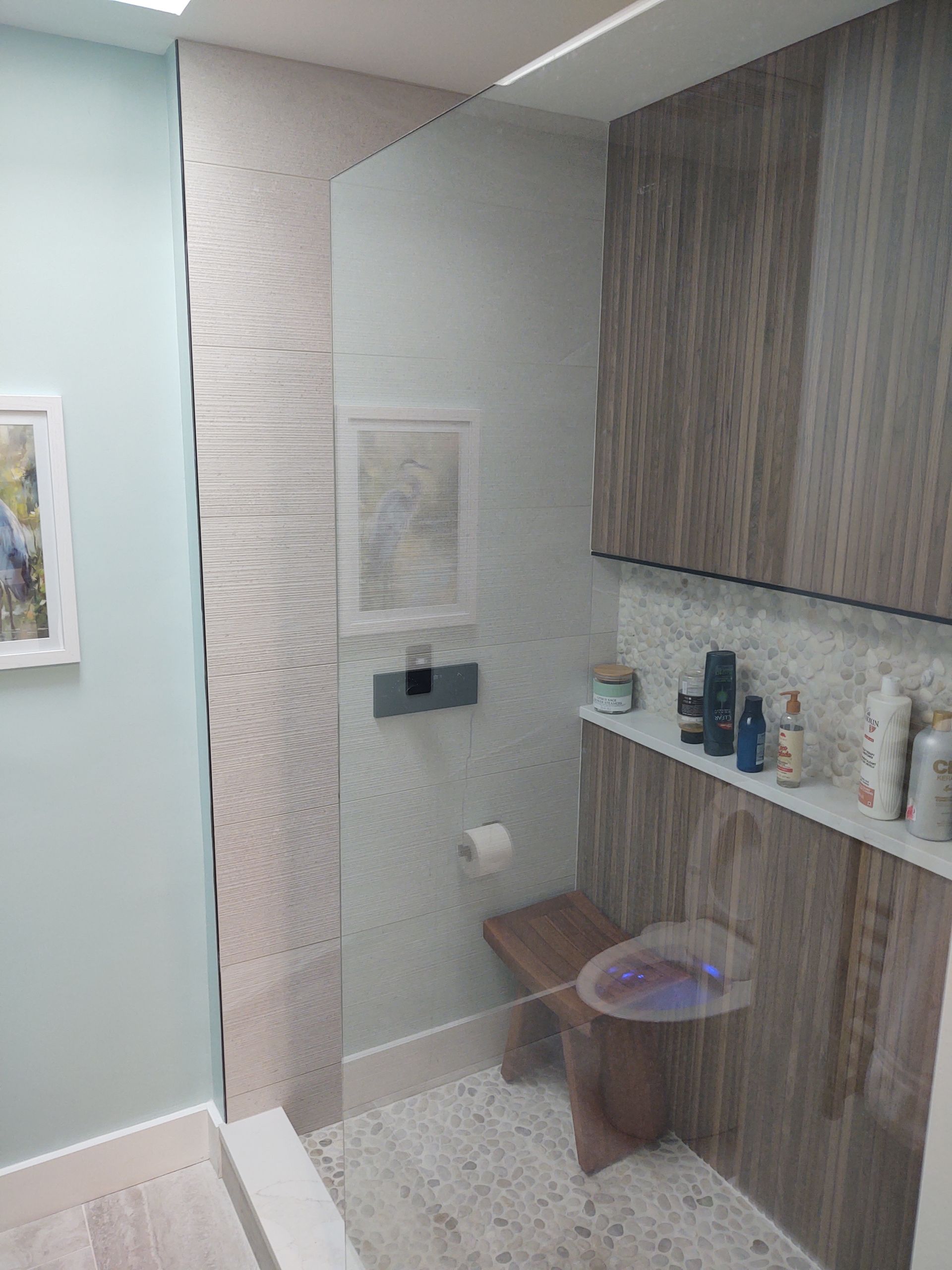 Bathroom interior with wood-look paneling, a toilet, a bench, and a shelf with toiletries.