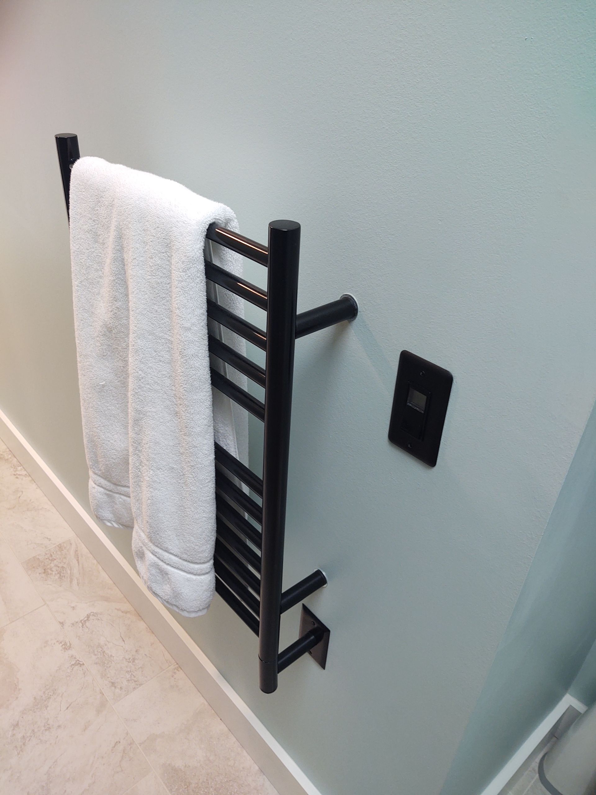 Black towel warmer with a white towel on a light green wall.