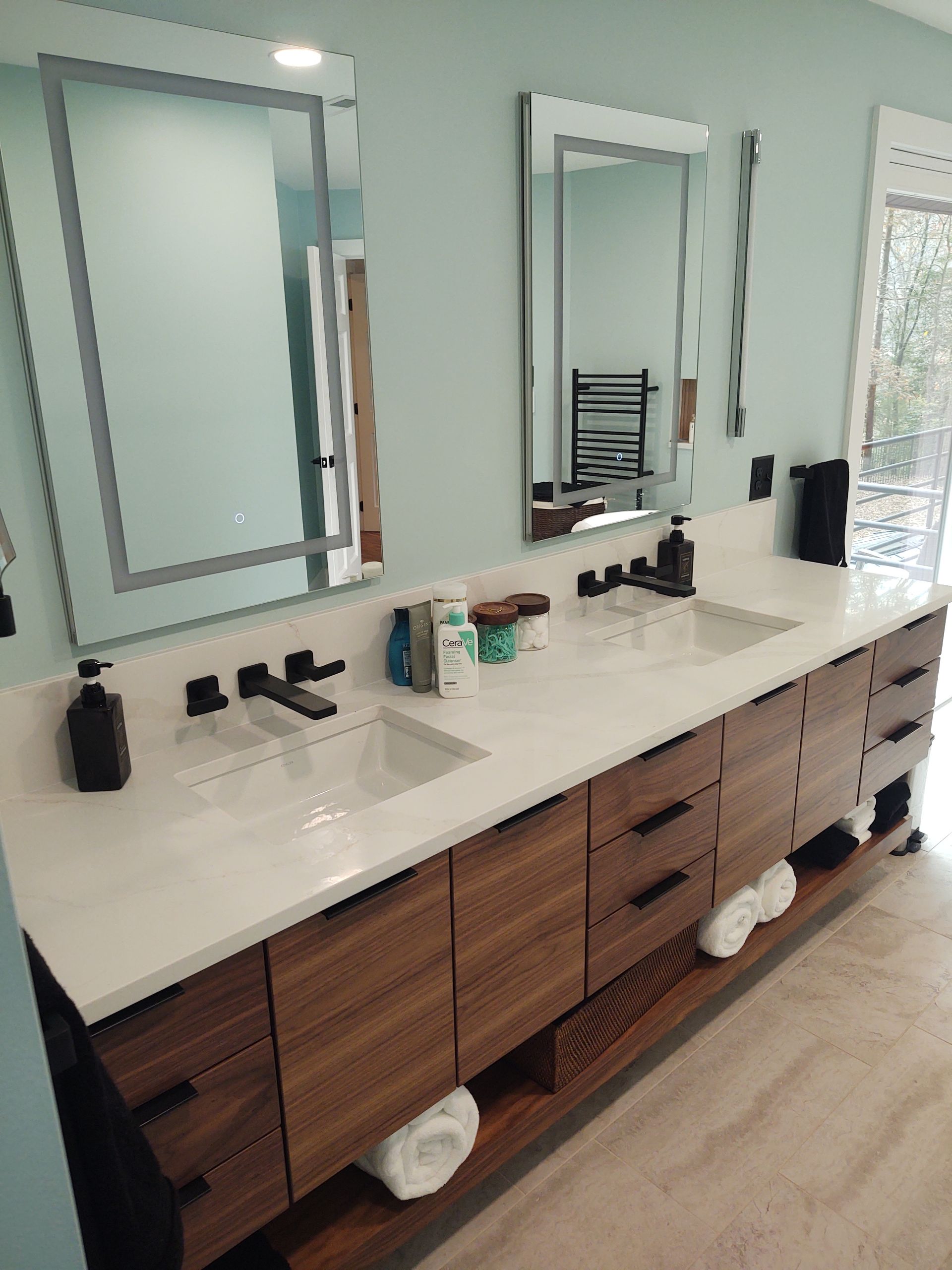 Bathroom with double vanity, walnut cabinets, white countertop, two mirrors, and black faucets against a light blue wall.