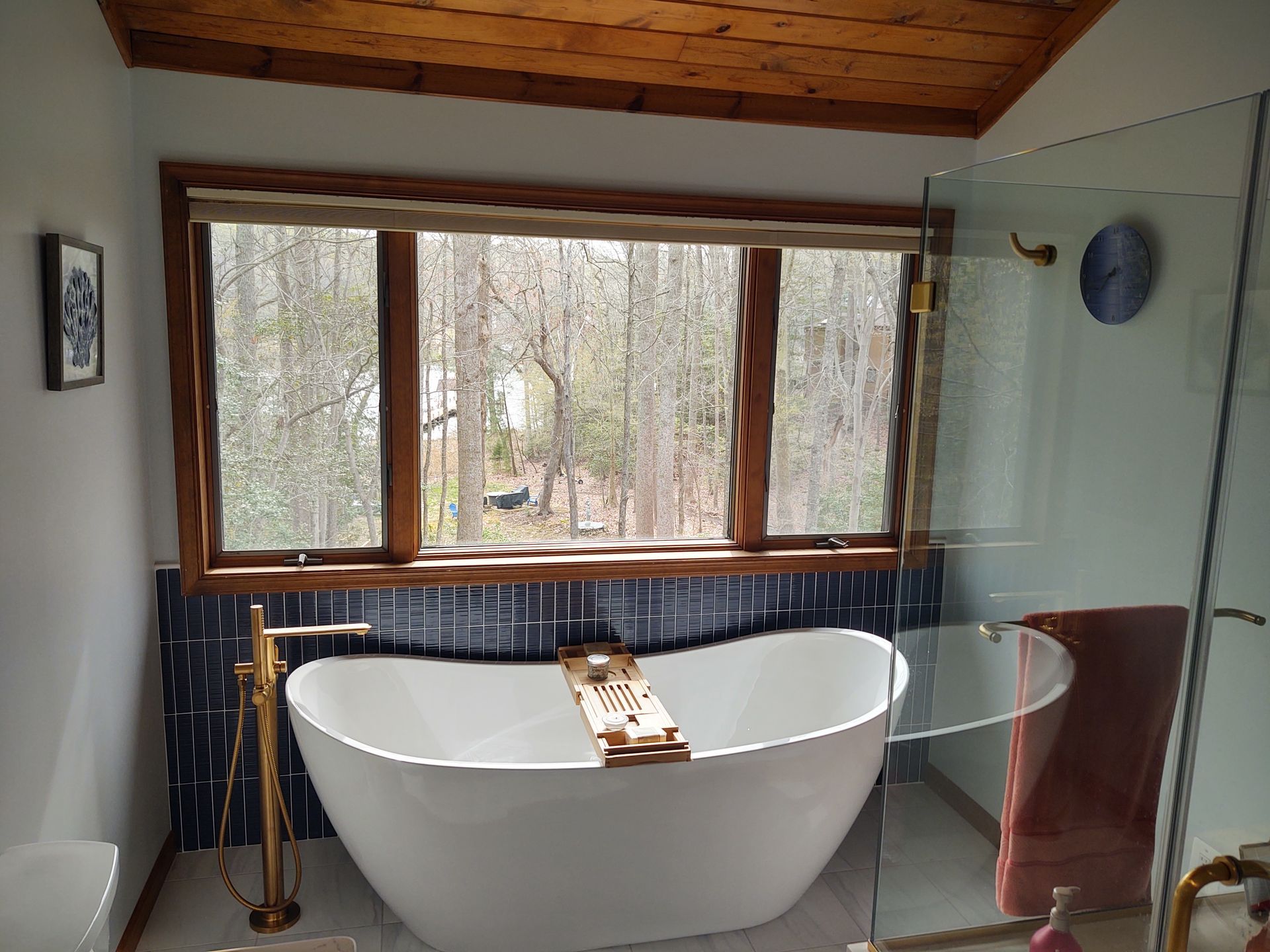 Bathroom with white tub, gold fixtures, window overlooking trees, dark blue tile.