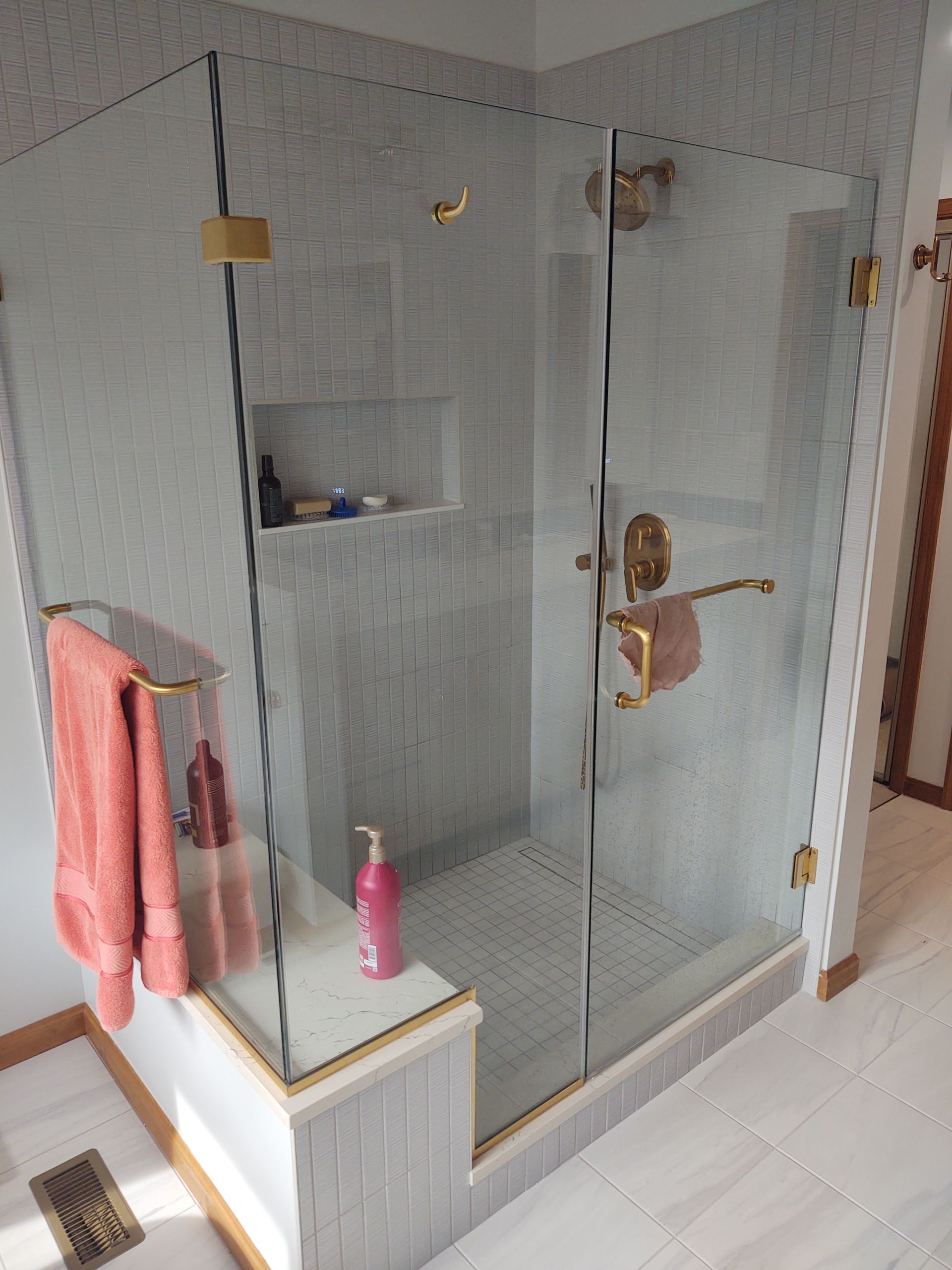 Glass shower enclosure with gold hardware, tiled walls, and a pink towel on a towel bar.