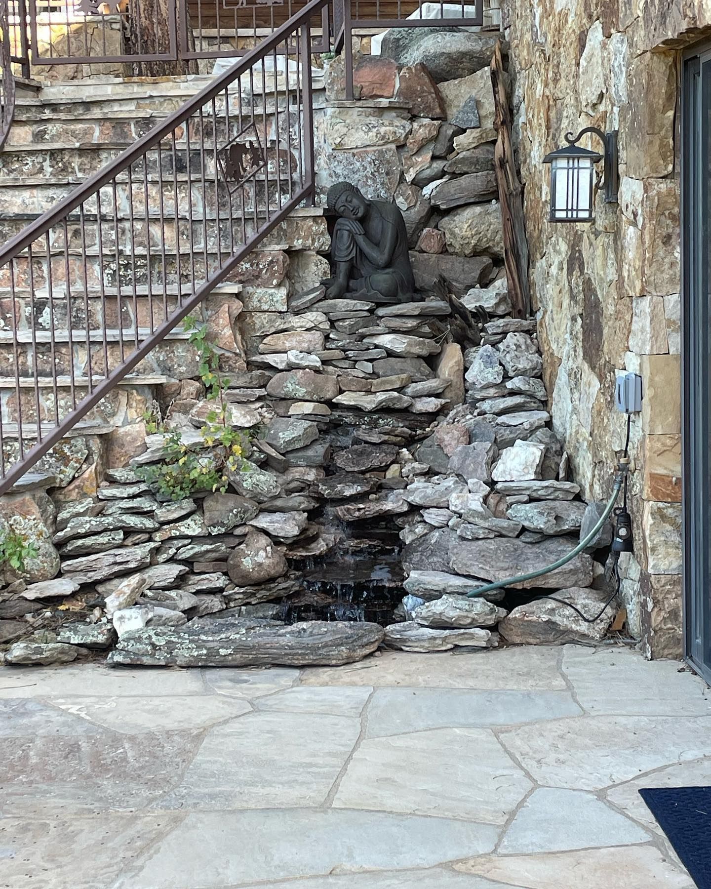Stone water feature with sculpture under exterior stairs.