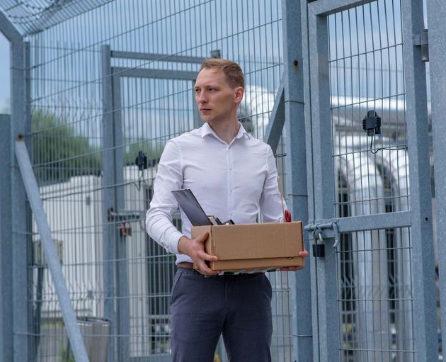 A man is holding a cardboard box in front of a fence.