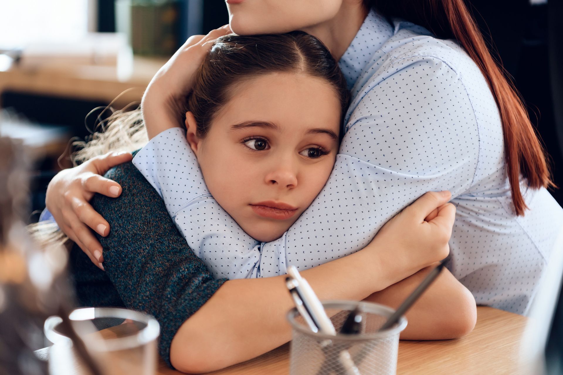 A woman is hugging a little girl who is sitting at a table.