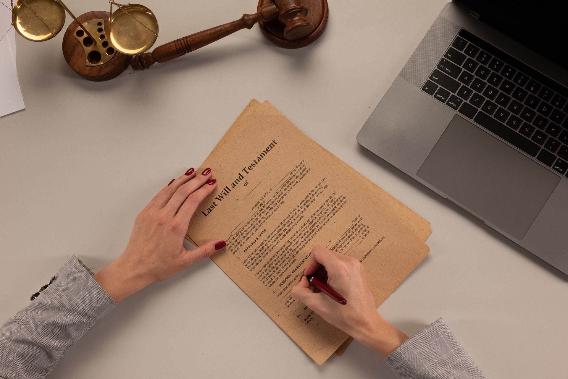 An attorney signing last will & testament papers on a desk with a gavel, scales of justice, & laptop