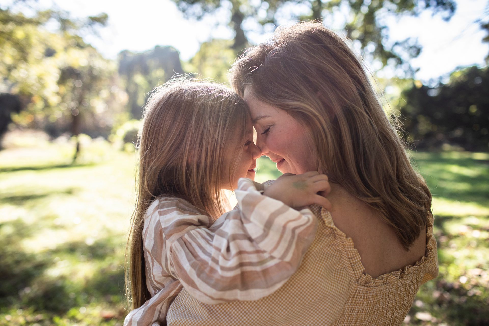 A woman is holding a little girl in her arms in a park.