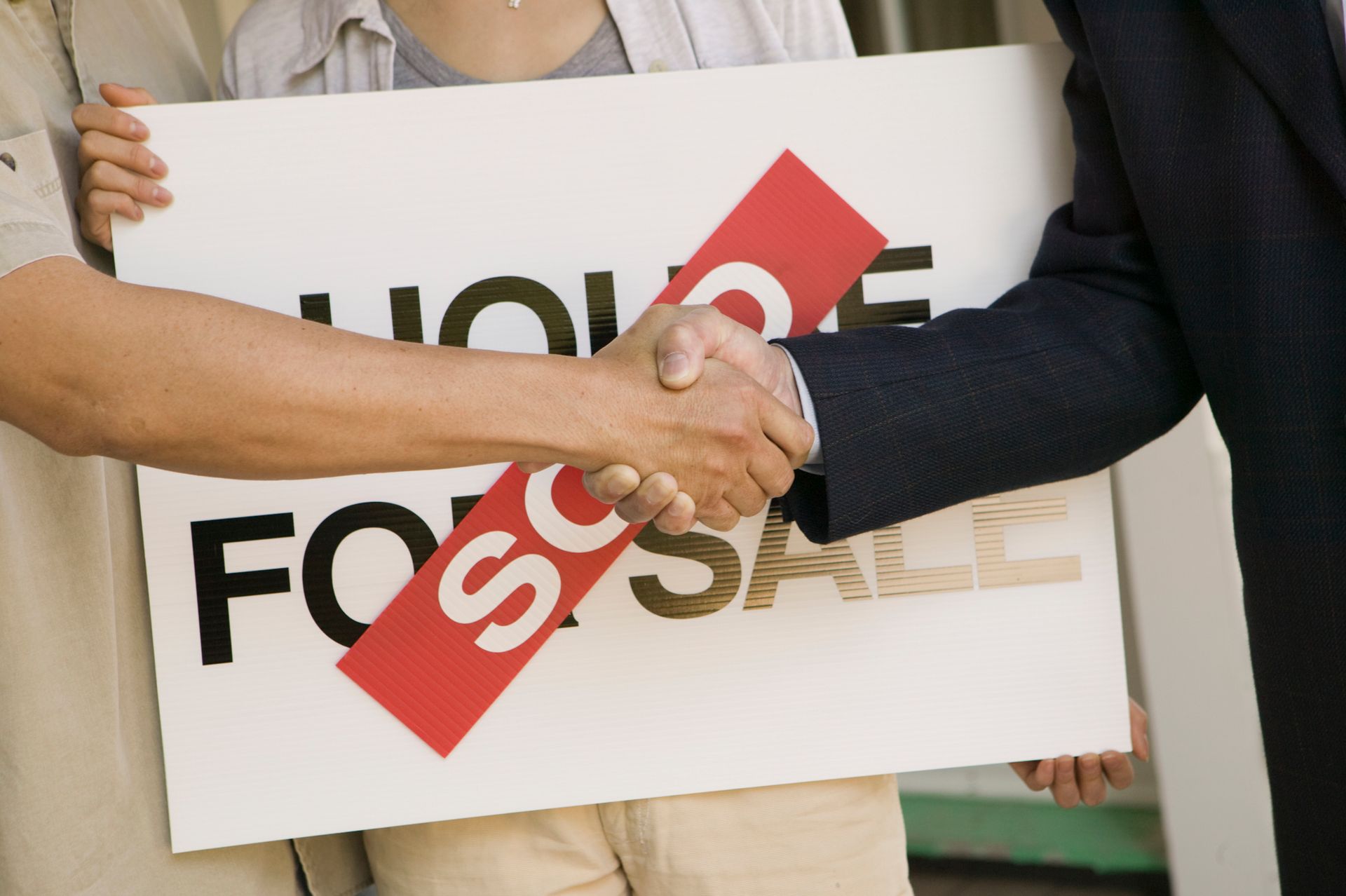Two people shaking hands while holding a sign that says for sale