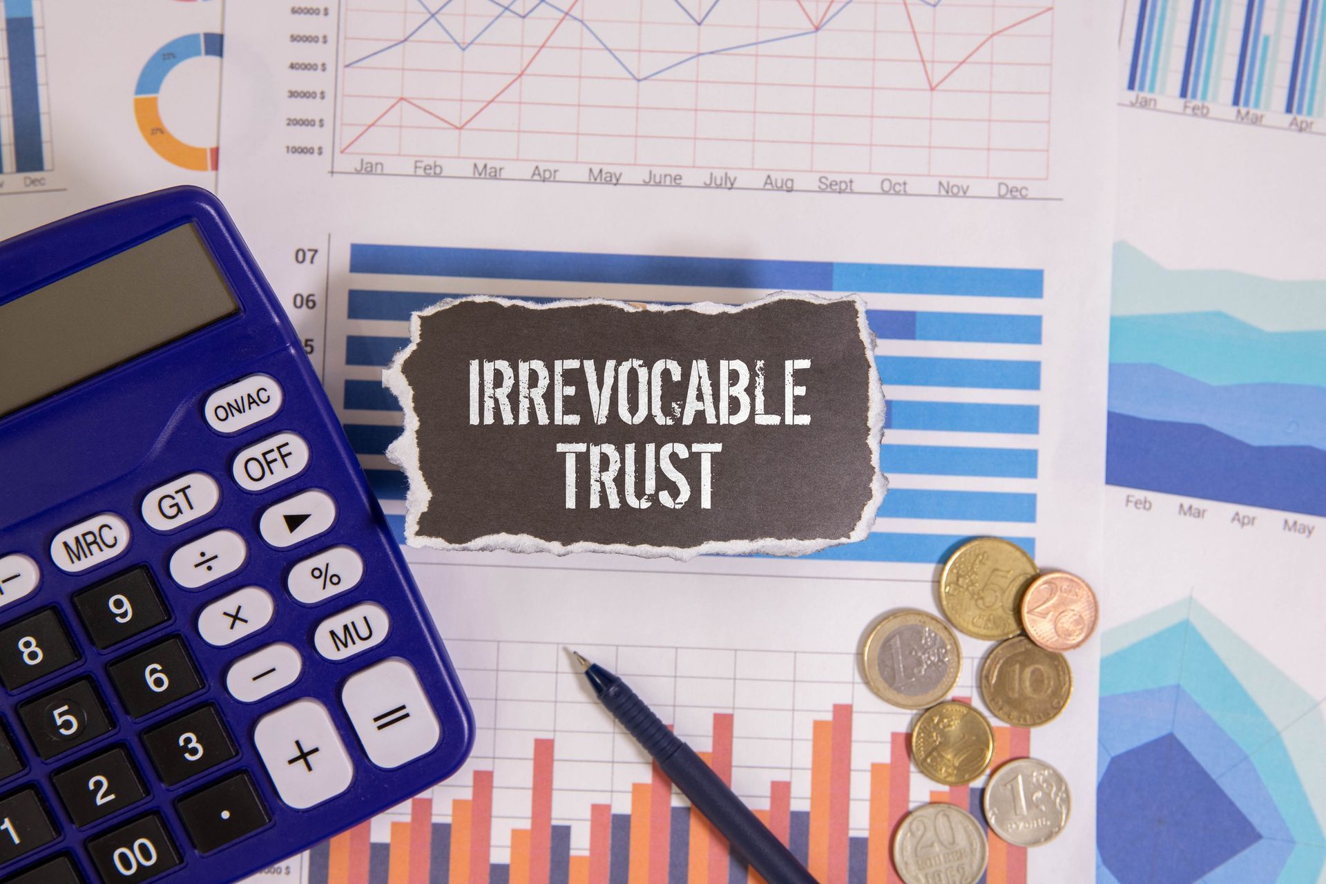 A calculator, pen, coins and a piece of paper with the words irrevocable trust written on it.