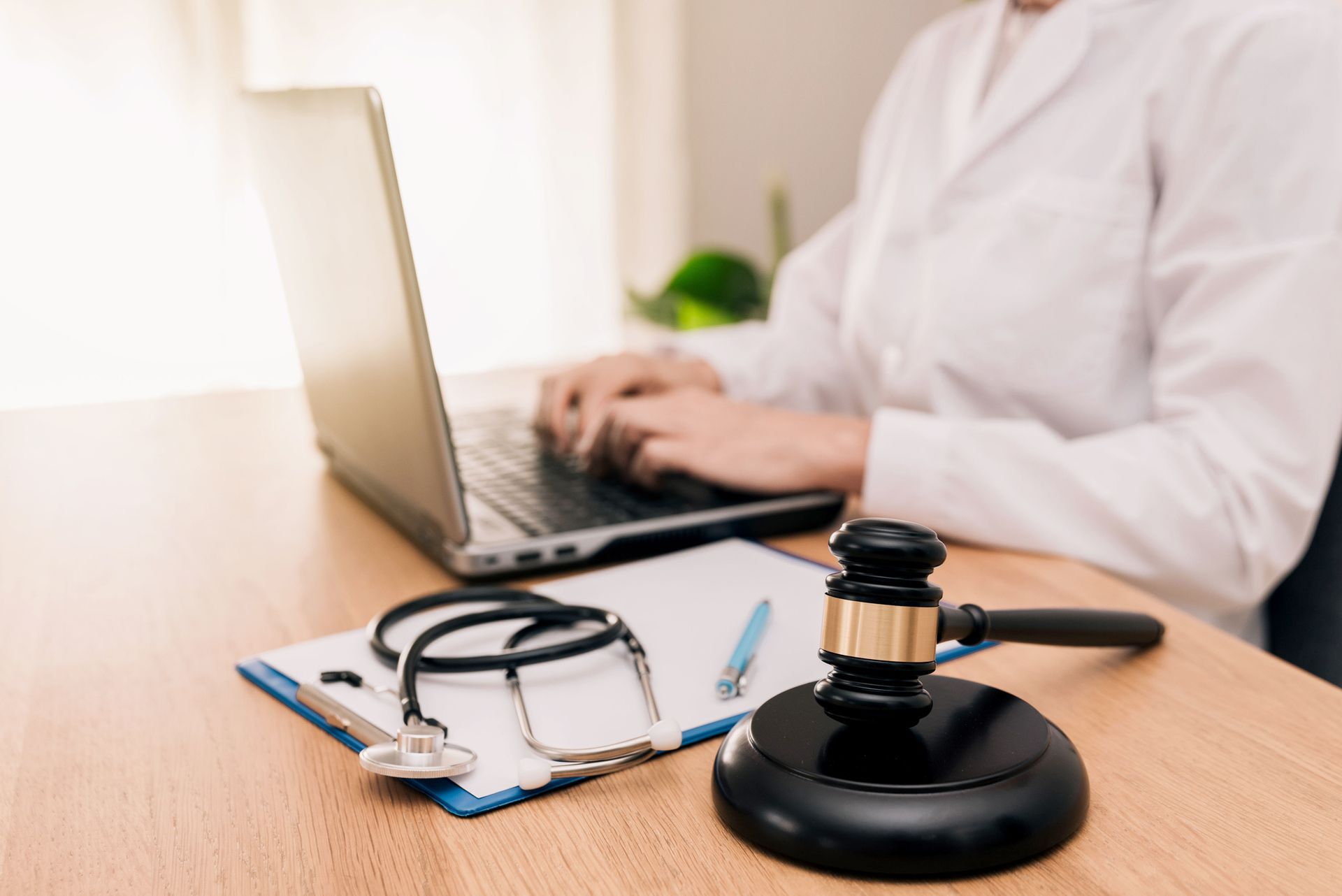 A doctor is typing on a laptop next to a stethoscope and a gavel.