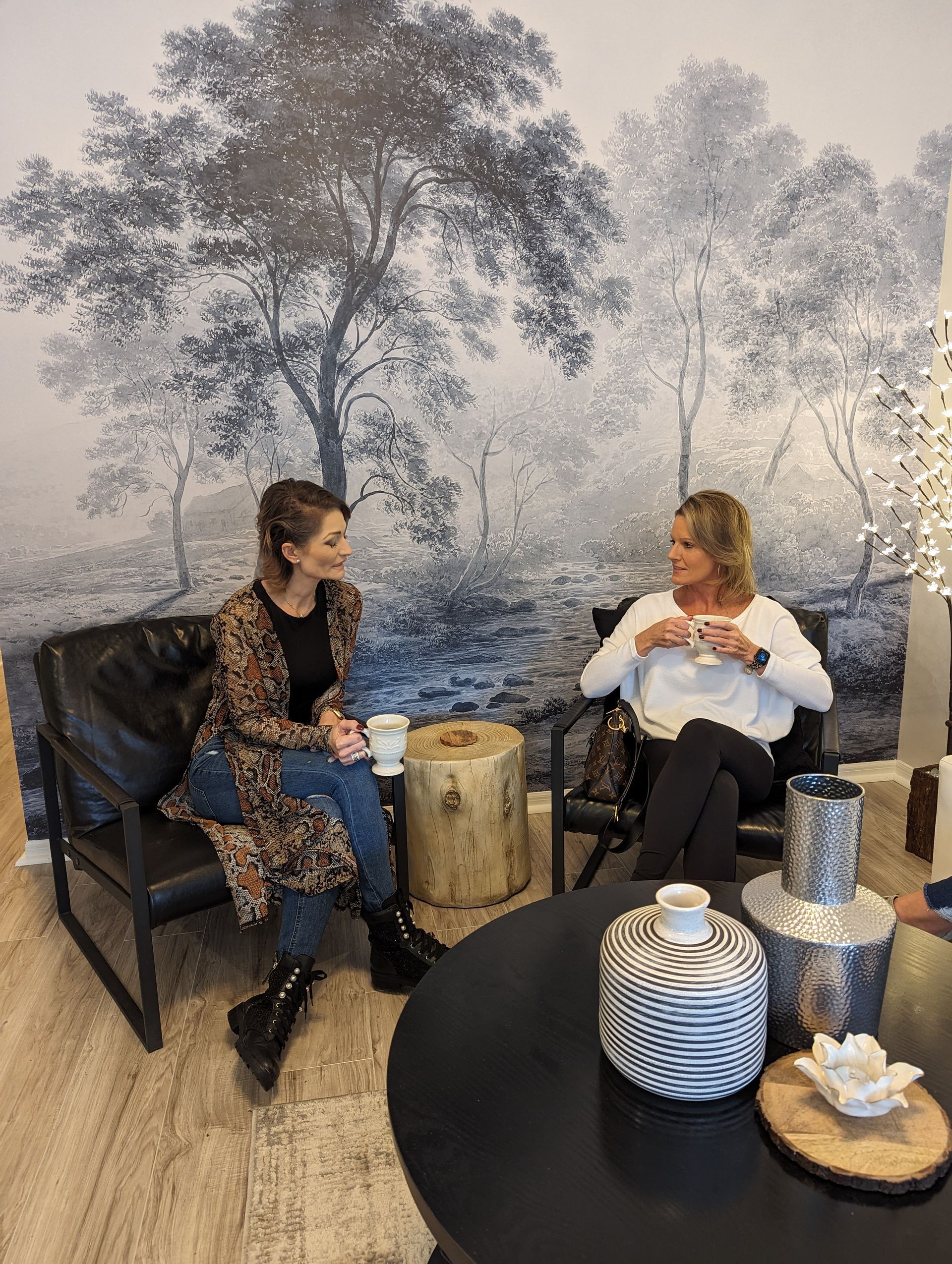 Two women are sitting in chairs in a living room drinking coffee.