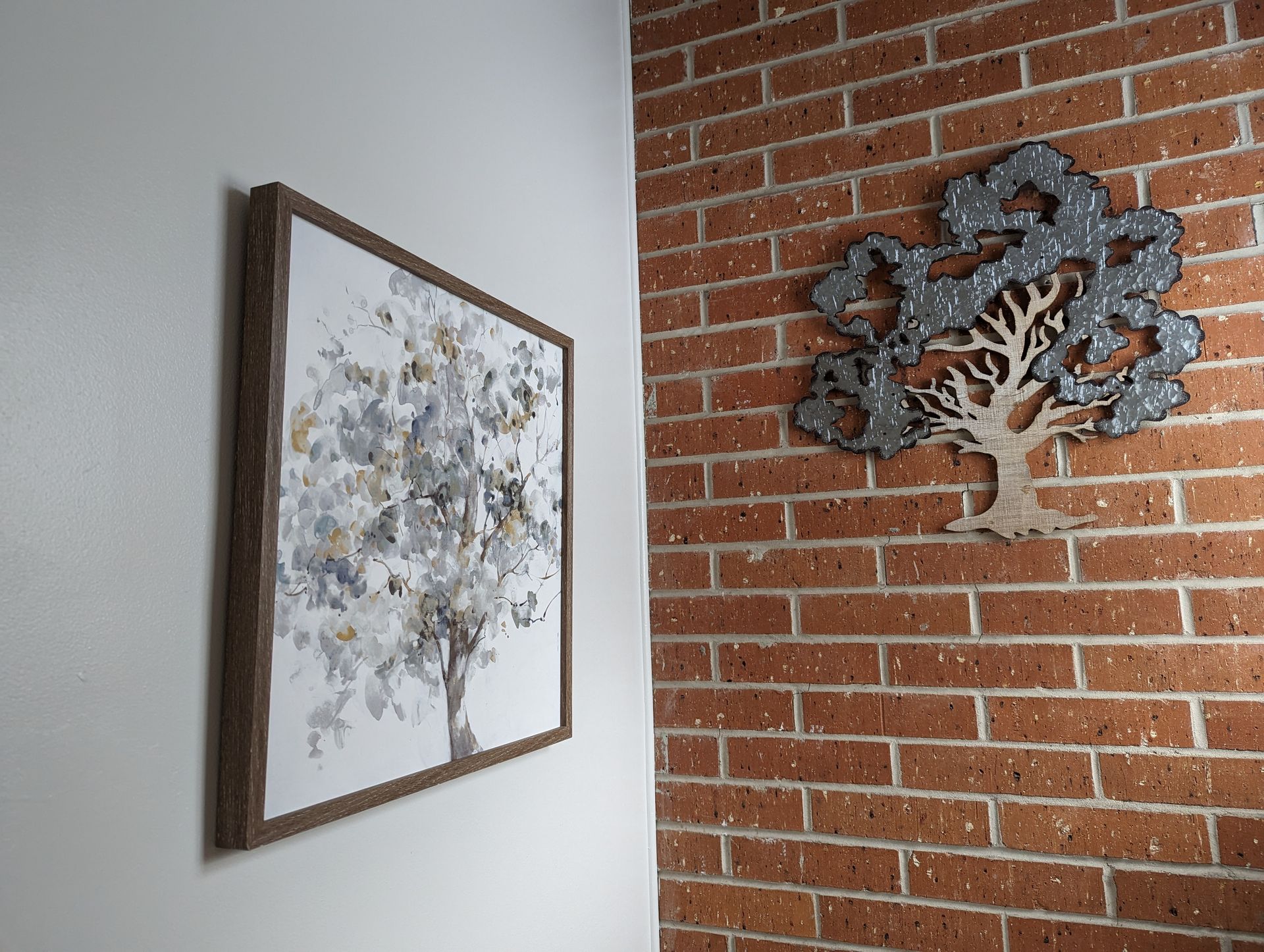 A picture of a tree is hanging on a brick wall next to a tree sculpture.