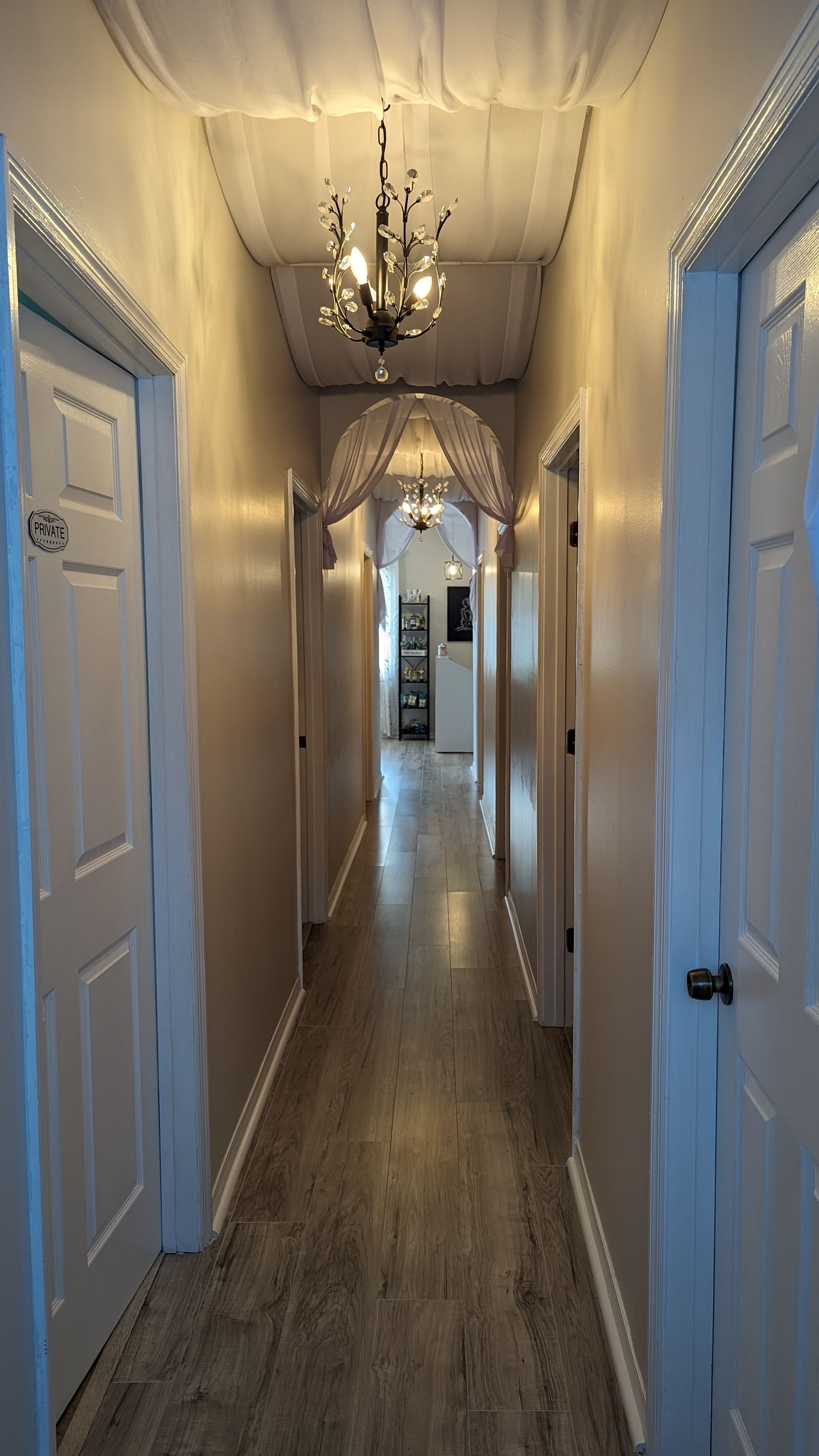 A long hallway with white doors and a chandelier hanging from the ceiling.