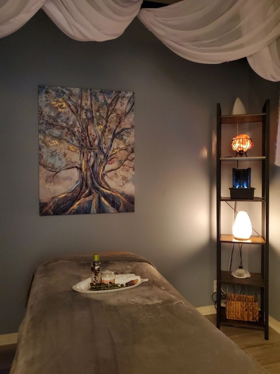 There is a painting of a tree on the wall above a massage table.