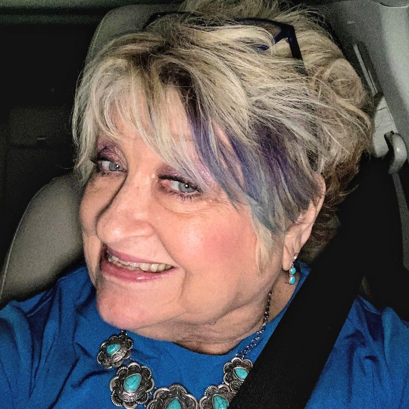 A woman wearing a blue shirt and a necklace is smiling while sitting in a car seat.