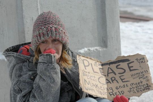 A woman is sitting in the snow holding a sign that says please care.