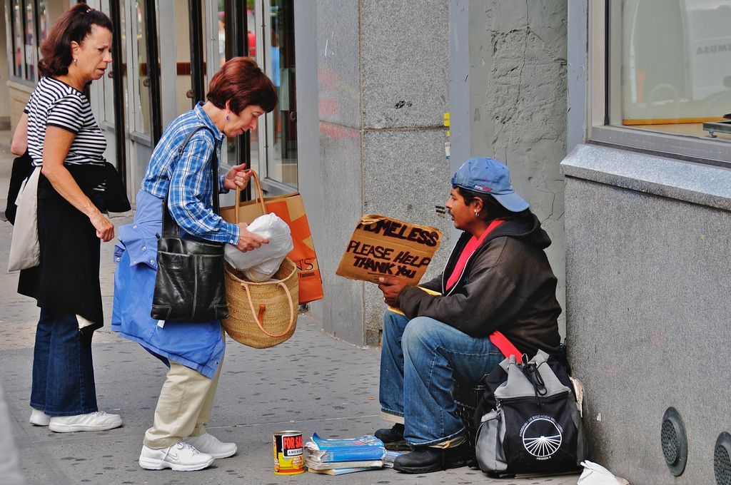 A man sitting on the sidewalk holding a sign that says purse