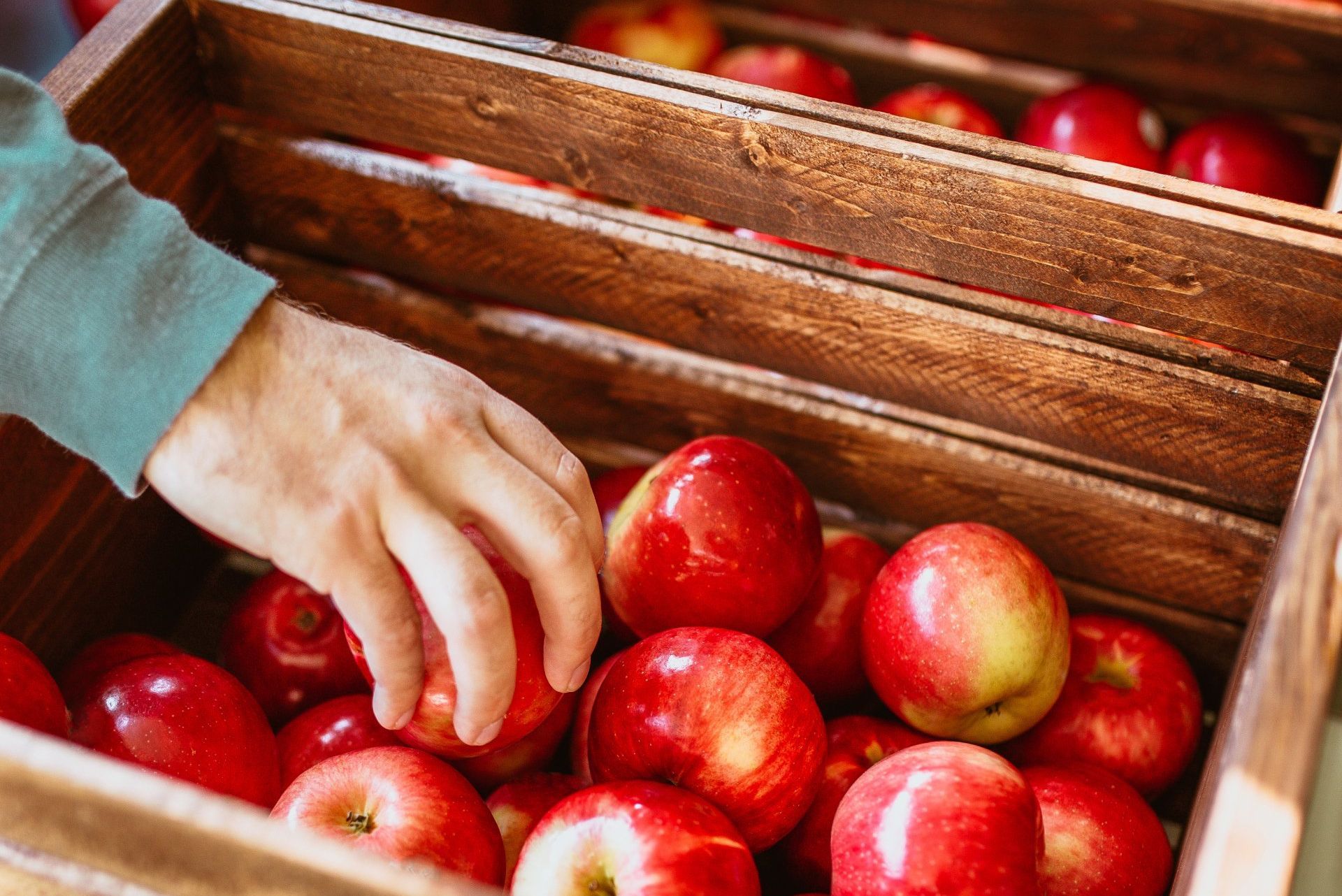 A person is picking apples from a wooden crate.