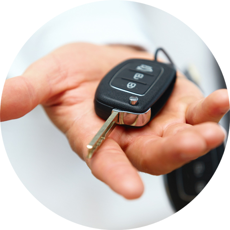 Hand holding a car remote, pointing it toward a car's open trunk.