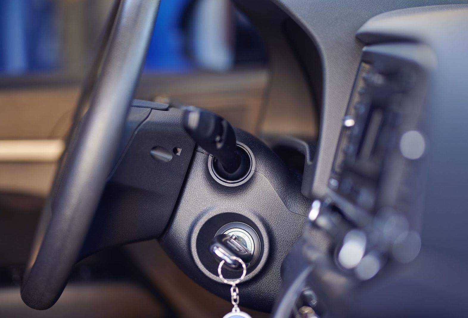Close-up of a car's ignition with a key inserted, next to the steering wheel and dashboard.