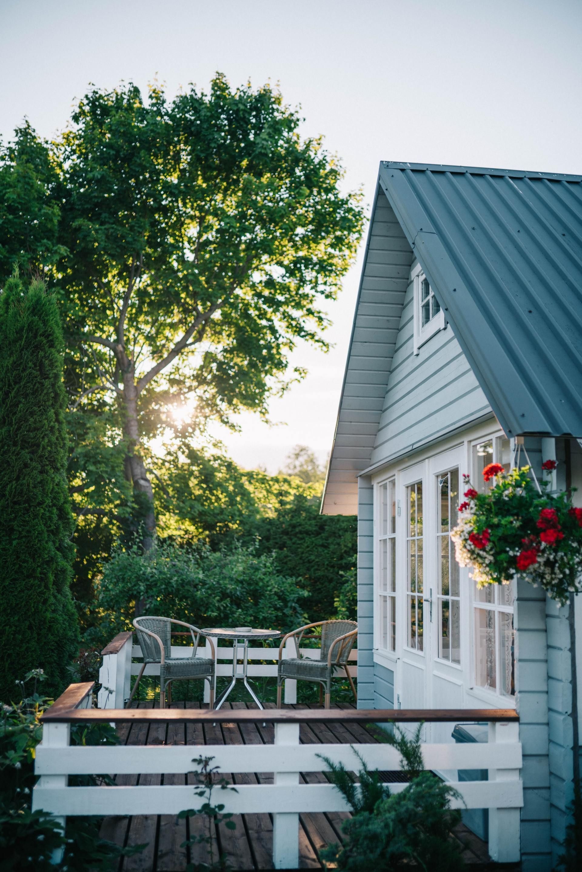 Blue and white cottage with deck and table surrounded by lush greenery at sunset.