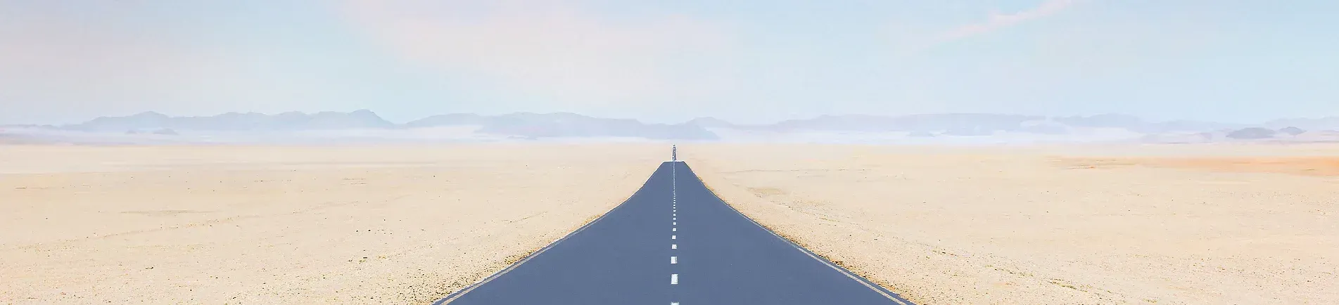 An empty road stretches to the horizon in a desert landscape under a blue sky.