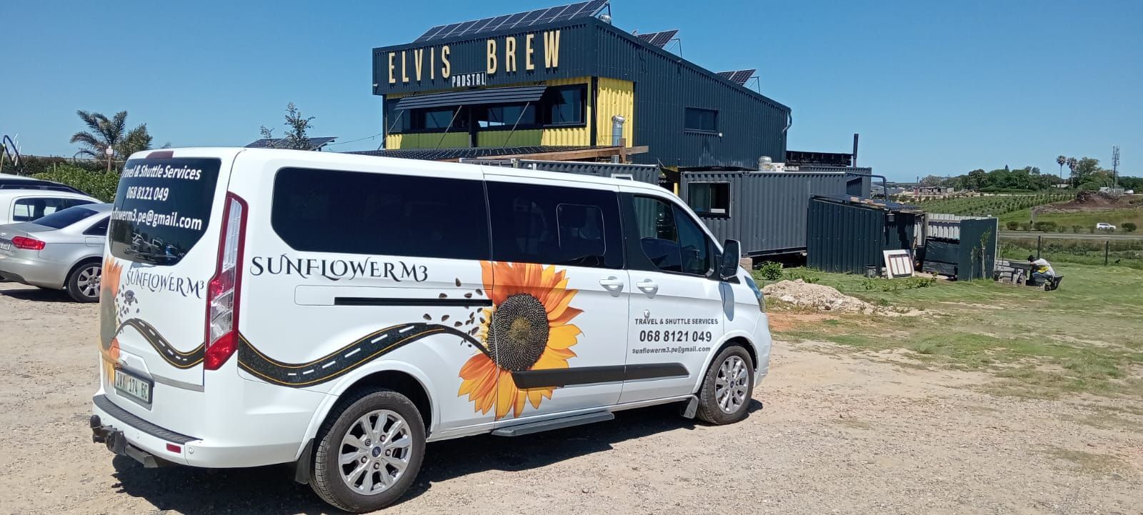 White van with a sunflower graphic parked near a rustic building with a 