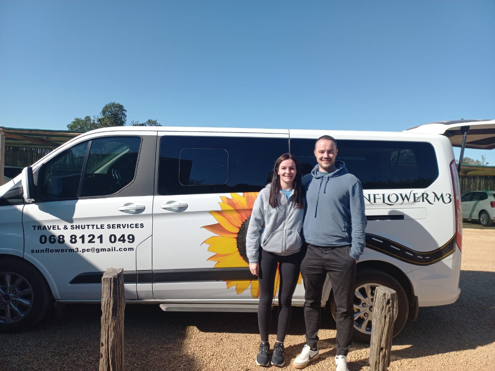 Two people standing by a white van with sunflower design. The van is labeled 