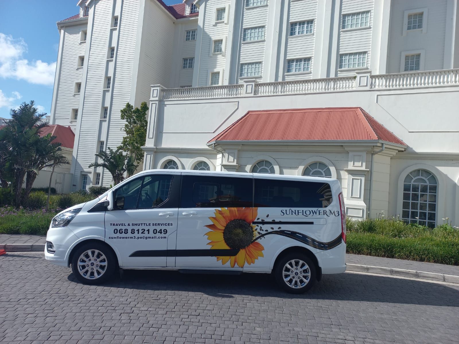 White van with sunflower graphic parked in front of a white building with red roof.