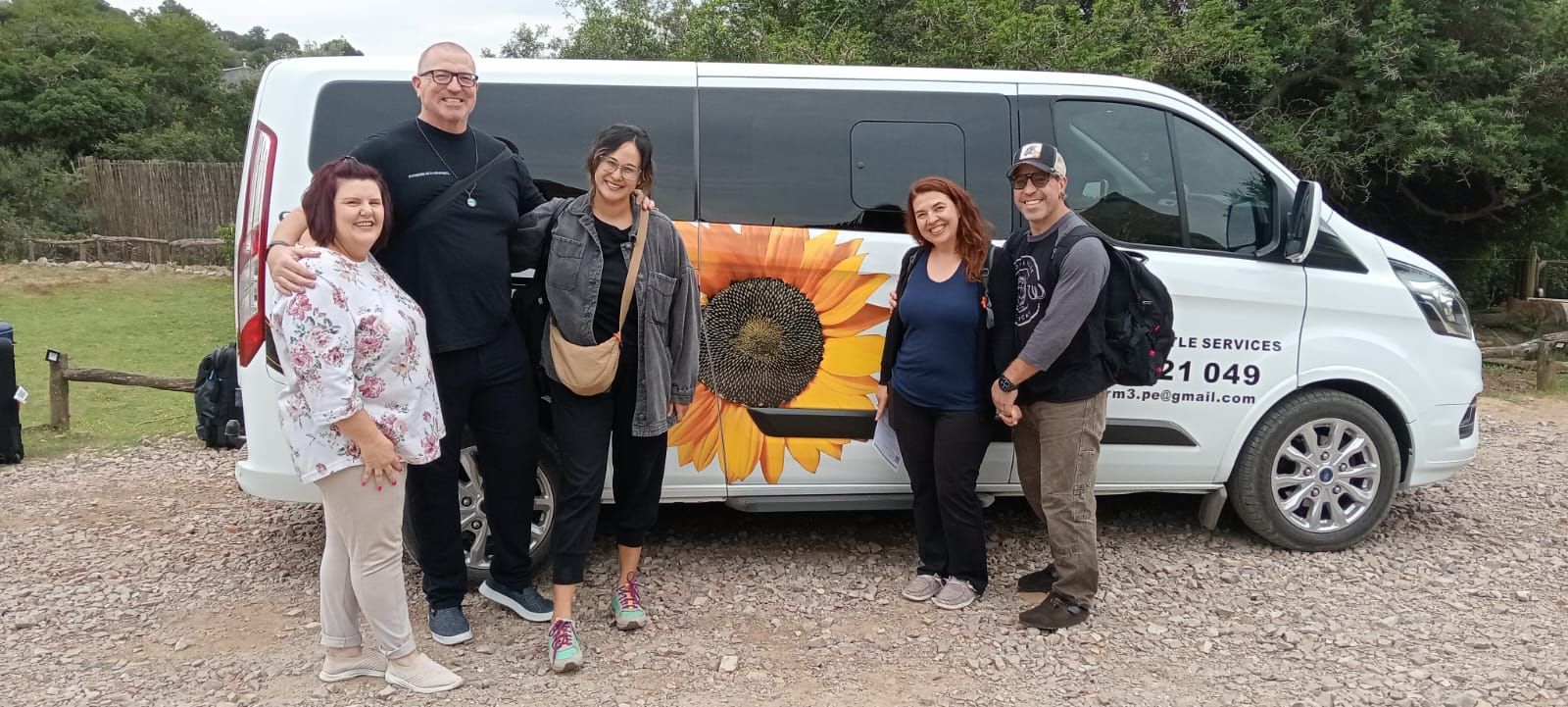 A group of five people standing in front of a white van with a sunflower graphic on it.