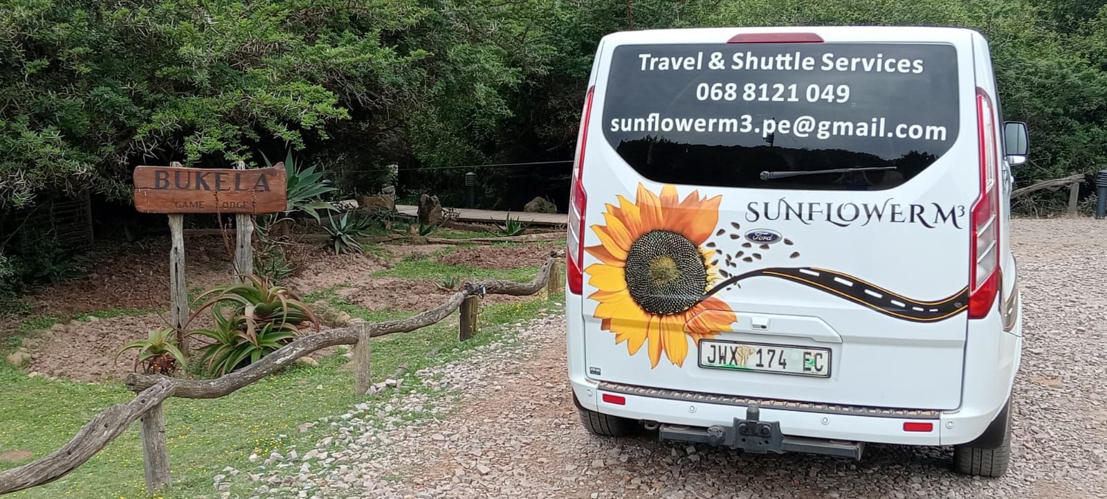 A white shuttle van with a sunflower design parked in front of a wooden sign that says 