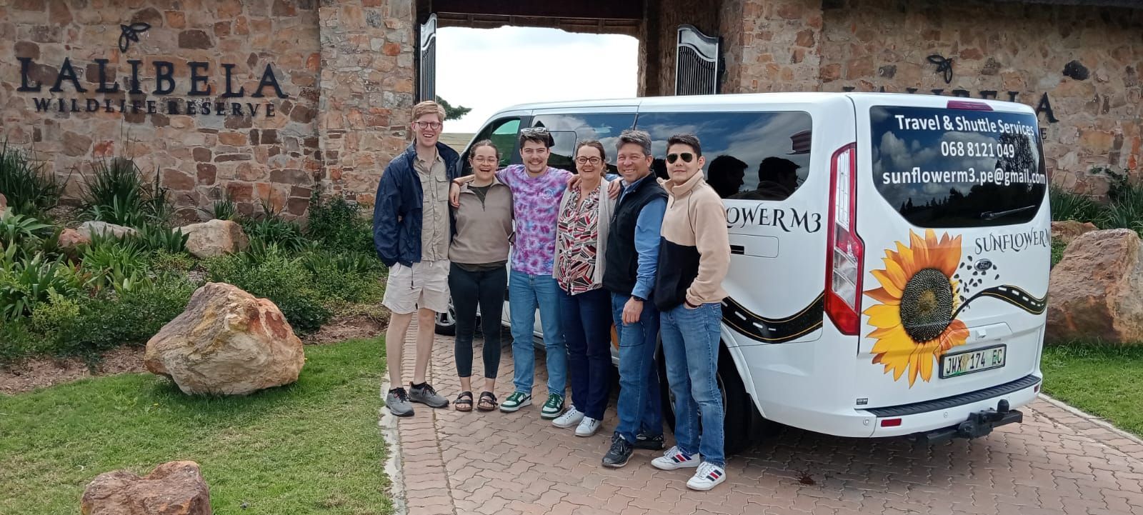 Group of people pose by a van decorated with a sunflower, in front of the Lalibela Wildlife Reserve.