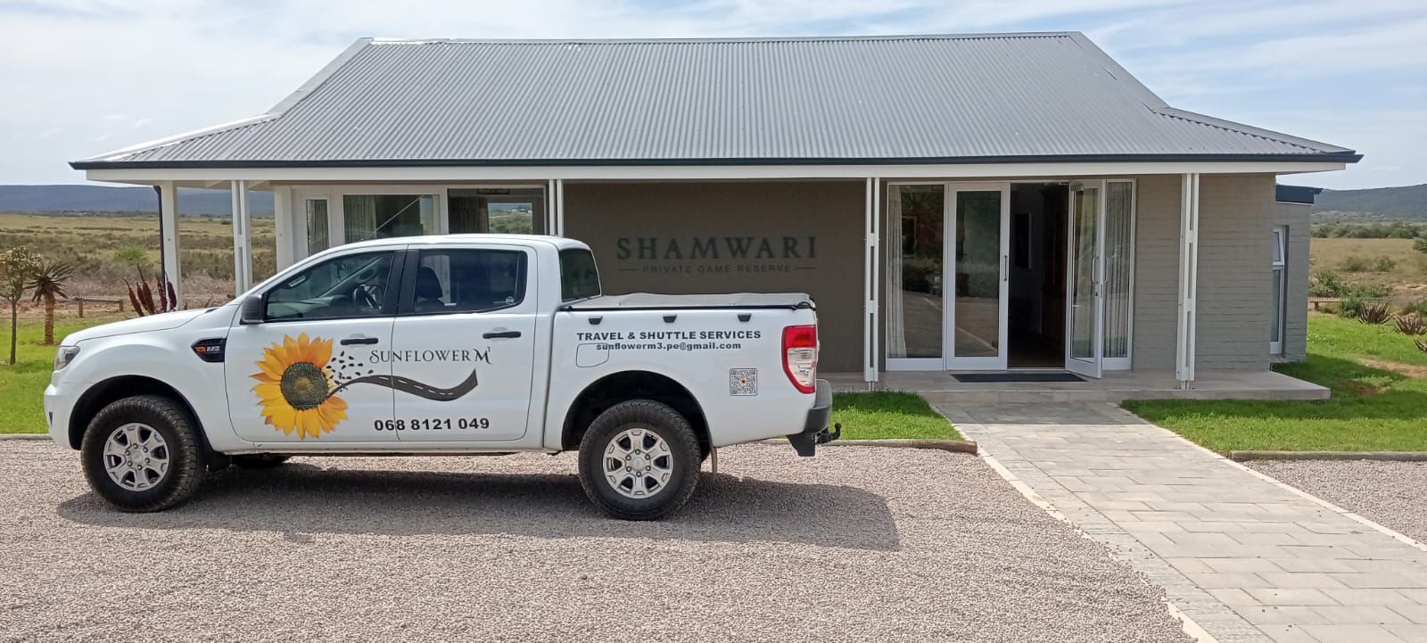 White pickup truck parked in front of a building with glass doors and a gray roof, gravel driveway.